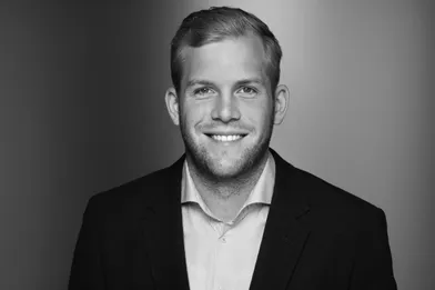 Porträt eines lächelnden jungen Mannes im Anzug vor neutralem Hintergrund. | MH Consulting